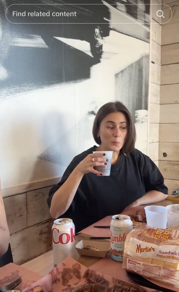 A woman in casual black attire drinks from a cup at a table with Diet Coke and Martin&#x27;s bread products