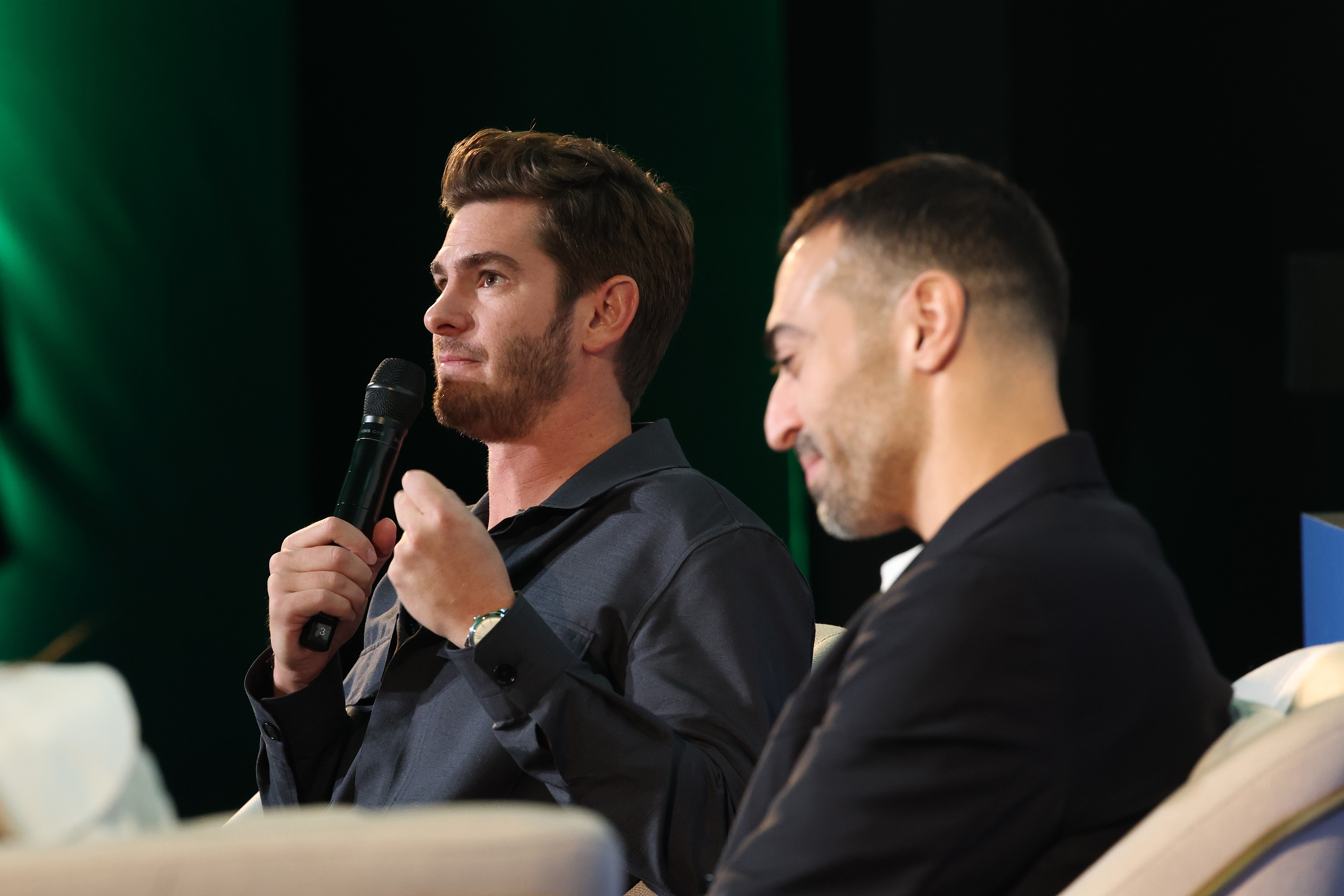Andrew Garfield speaks into a microphone while seated onstage