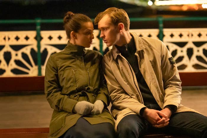 Two people on a bench wearing coats gaze at each other closely