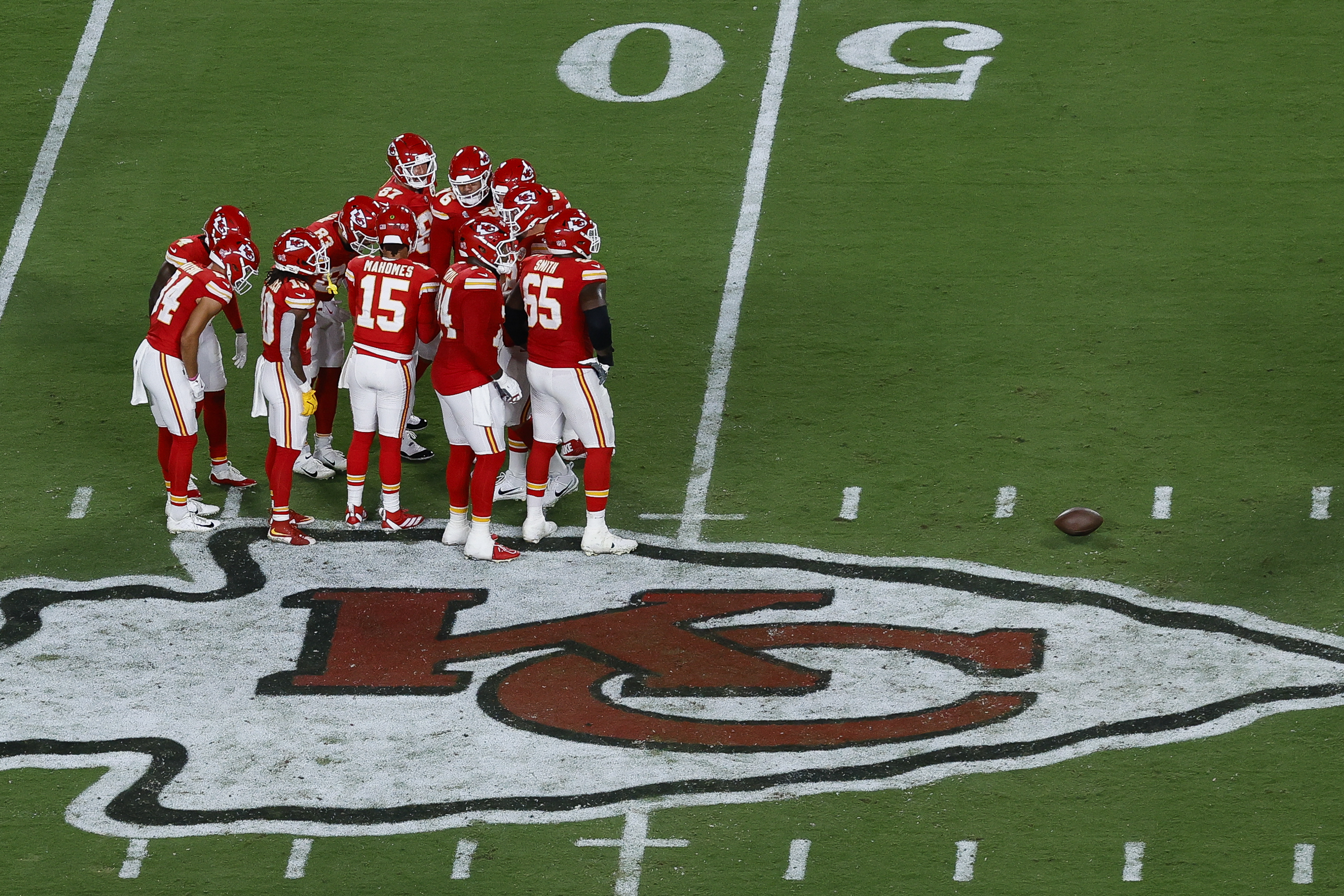 Kansas City Chiefs players huddle on a field with the team logo at midfield