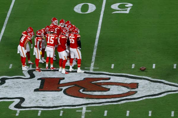 Kansas City Chiefs players huddle on a field with the team logo at midfield