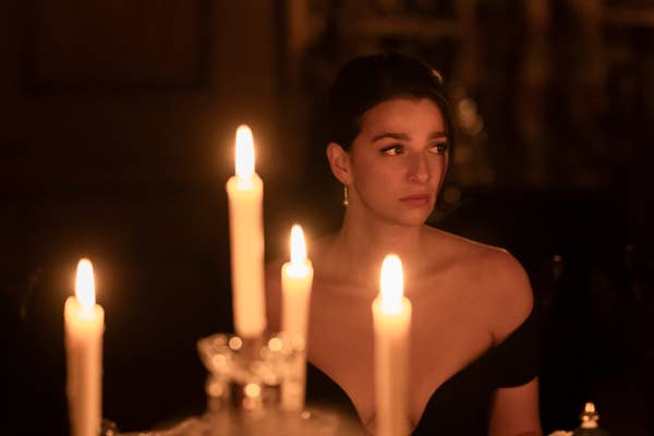 I don&#x27;t know who is in the image. A woman with short dark hair, wearing an off-the-shoulder dress, is sitting at a table with lit candles