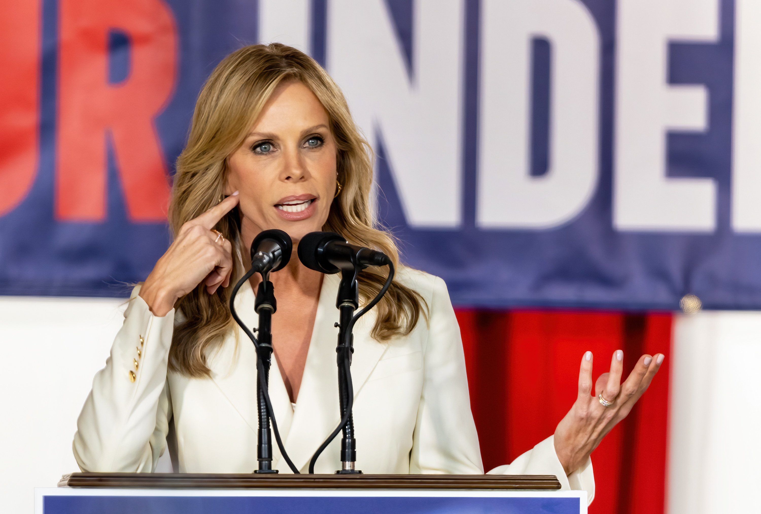 A woman speaks passionately at a podium with a banner behind her