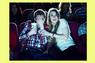 Two people in a movie theater, looking startled. One covers their face with their hand, while the other watches the screen wide-eyed
