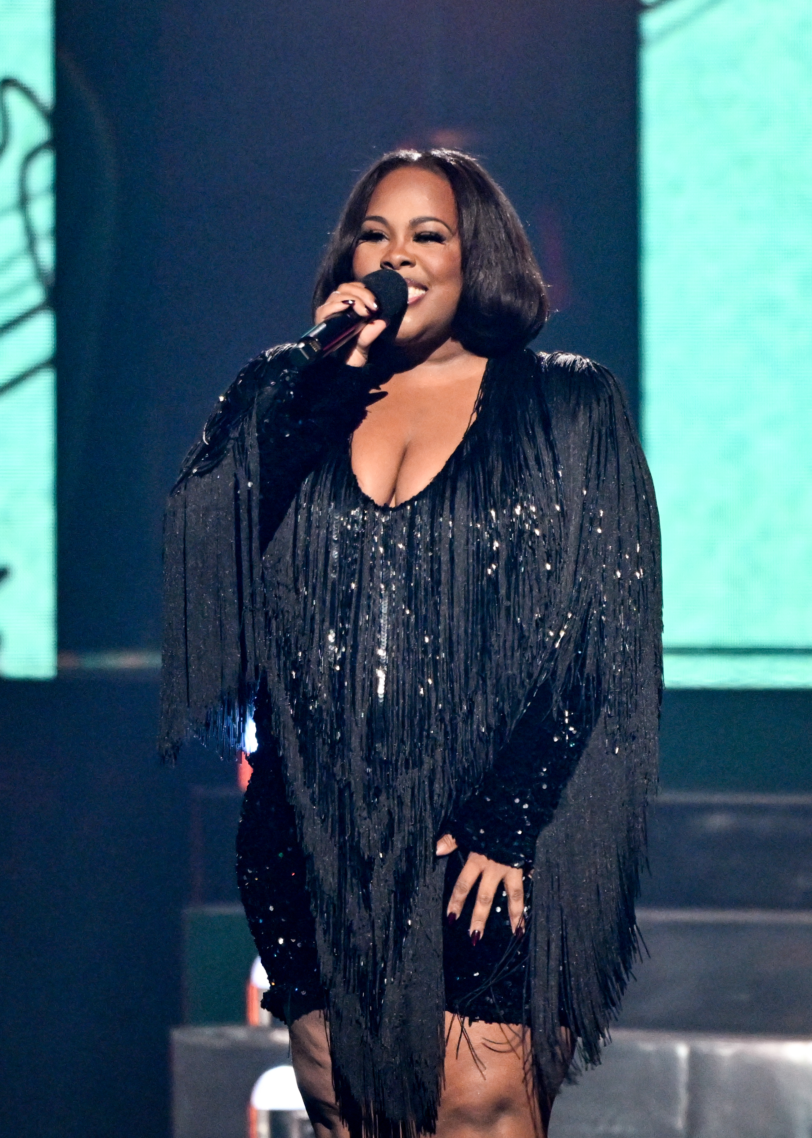 Singer in fringed, shimmering outfit performs on stage with a microphone