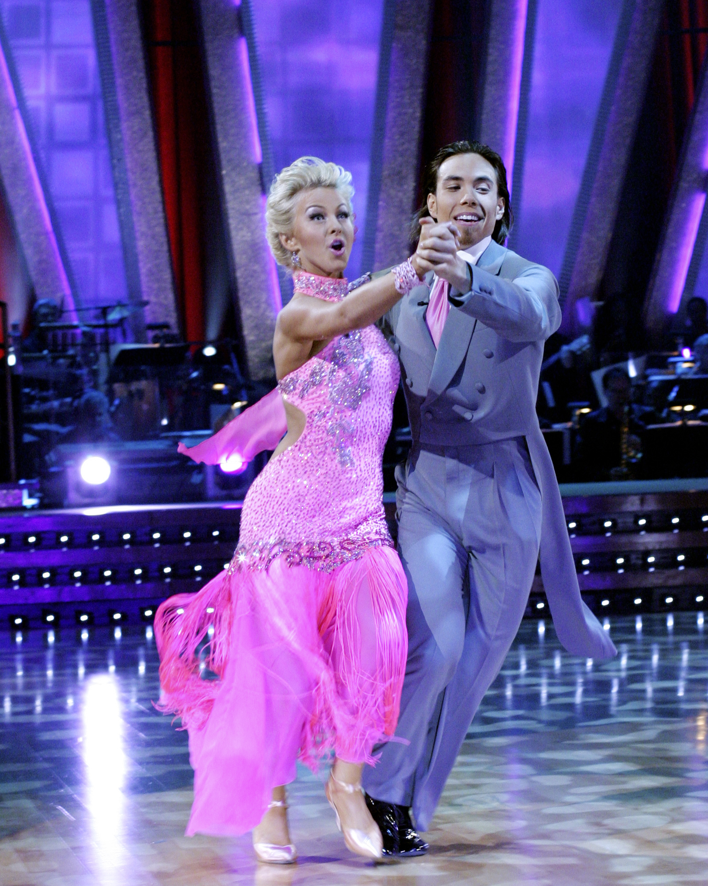 Apolo Ohno and Julianne Hough are dancing in formal attire on a stage; the woman wears a fringed dress, and the man is in a suit