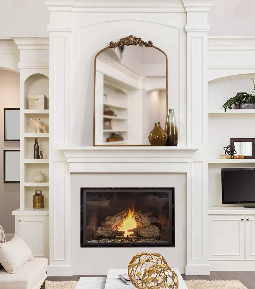 Elegant living room with a central fireplace, decorative mirror, and built-in shelves displaying various vases and decor items