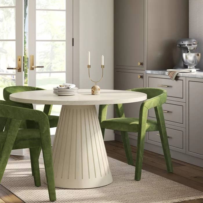 Modern dining room with a round table, green chairs, and a mixer on the counter, featured in a shopping article
