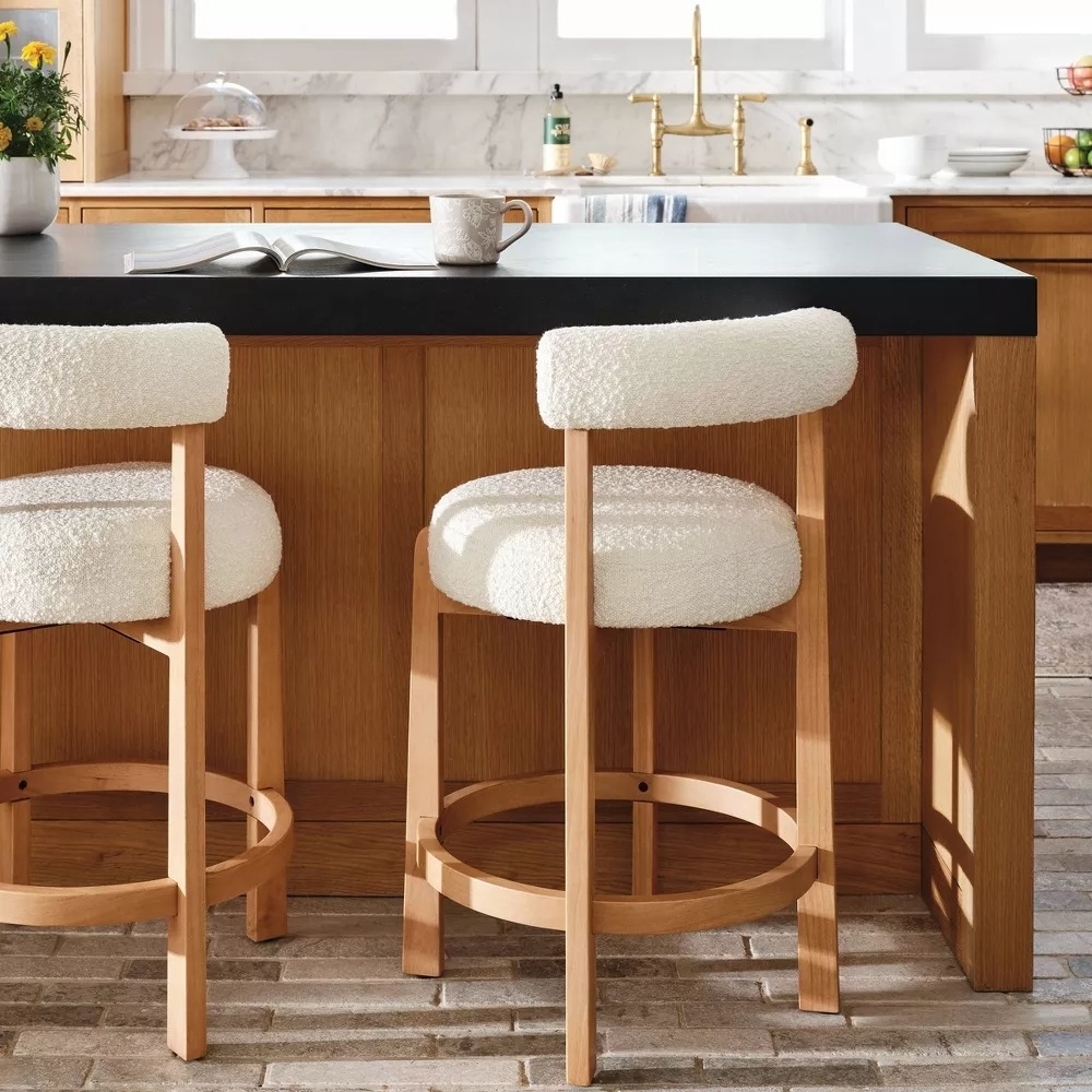 Two modern barstools with cushioned white seats at a kitchen island, set in a stylish kitchen with wooden cabinets and decor