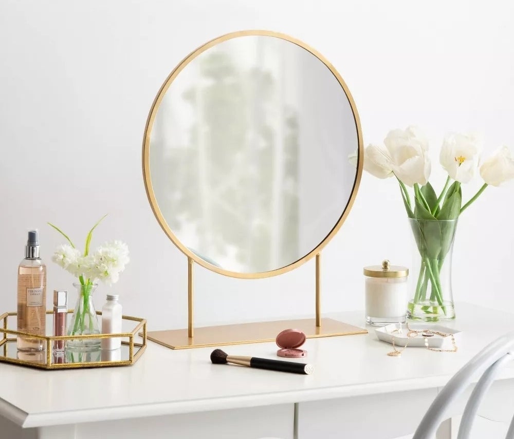 Vanity with round mirror, makeup brushes, perfumes, and a vase of tulips on a white table, creating a chic and organized beauty space