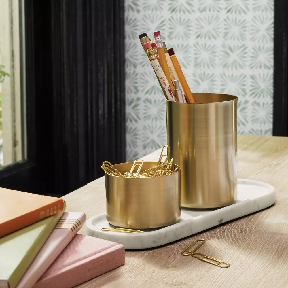 Gold desk organizers with pencils and paperclips, stacked books on a tabletop