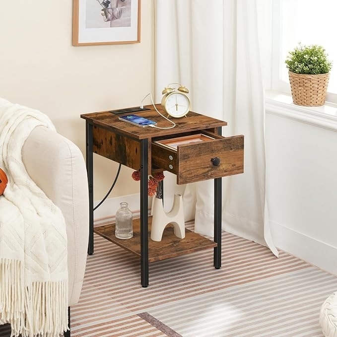 Wooden side table with a drawer open, clock, and phone on top; white sofa and a potted plant nearby, showcased in a cozy living room setting