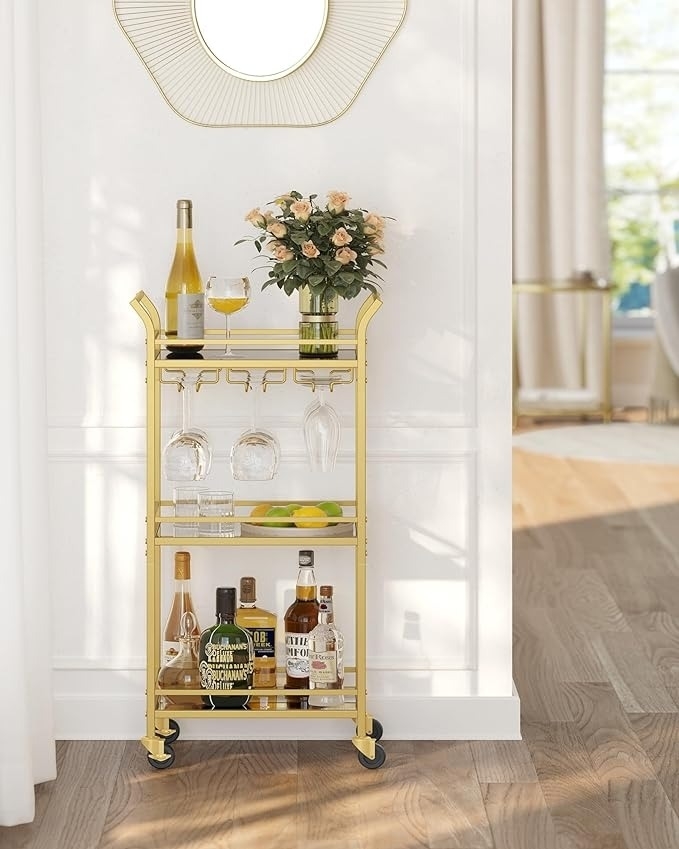 Bar cart with wine, spirits, glasses, and flowers, set in a home with a wall mirror above. Elegant and organized for home shopping inspiration