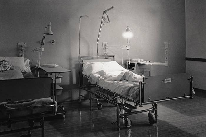 Hospital room with an empty bed, nightstand, and medical equipment. Dimly lit, creating a calm yet somber atmosphere