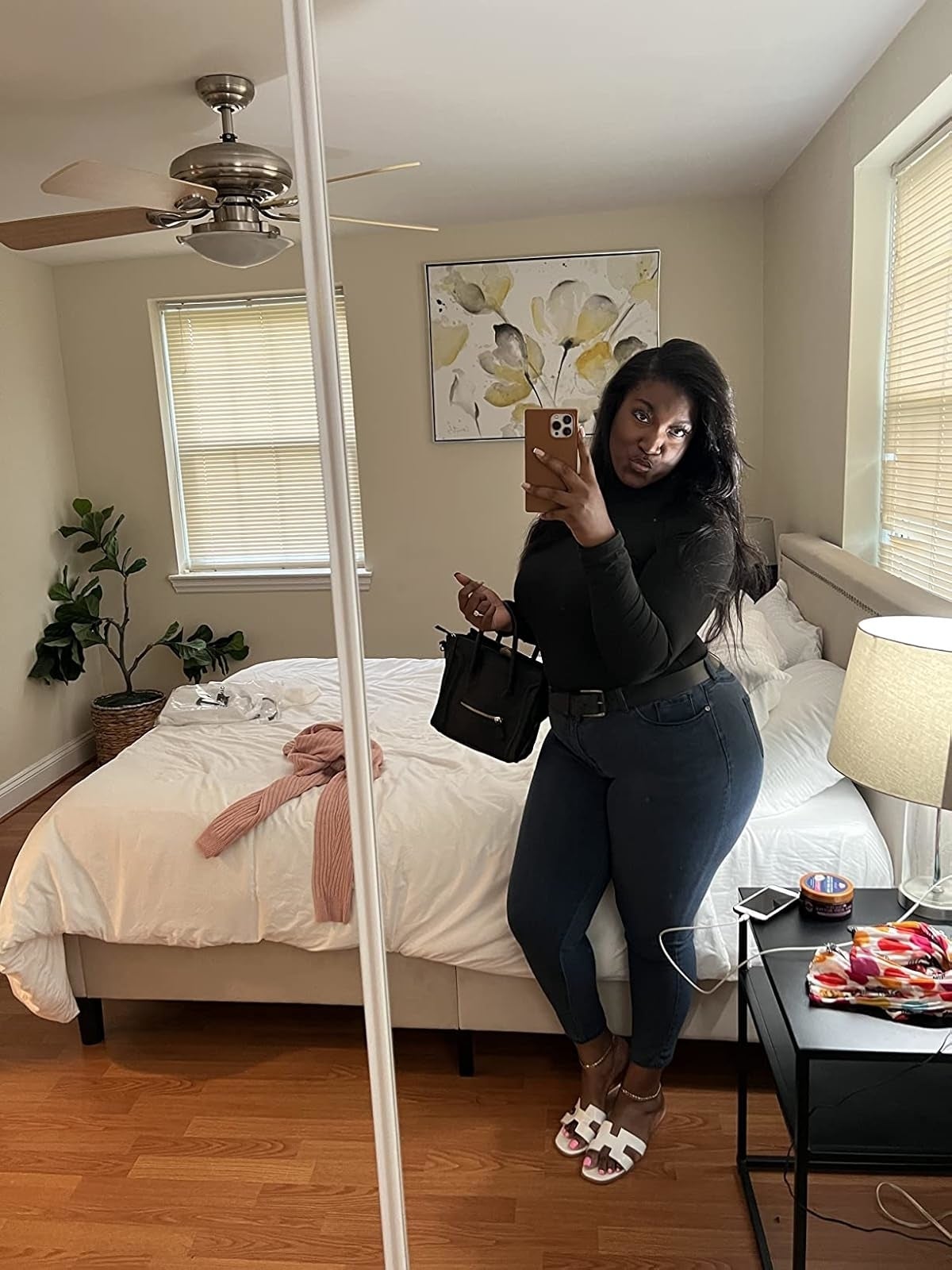 Reviewer successful  a chamber  reflector  selfie wearing a achromatic  top, faux leather leggings, and achromatic  sandals, holding a achromatic  bag.