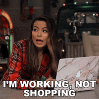 Miranda Cosgrove looks surprised while sitting in front of a laptop, with the text &quot;I&#x27;m working, not shopping&quot; above her