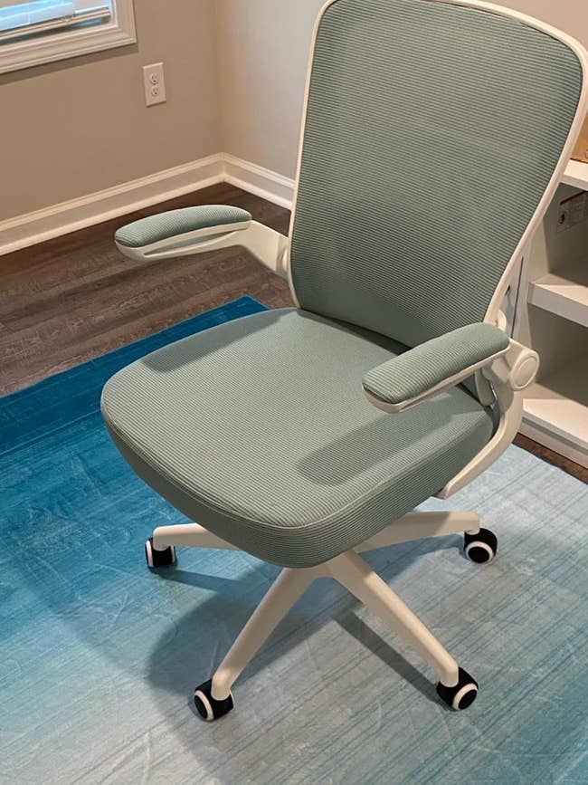 reviewer's ergonomic bureau seat with adjustable armrests and swivel wheels connected a bluish rug successful a location bureau setting
