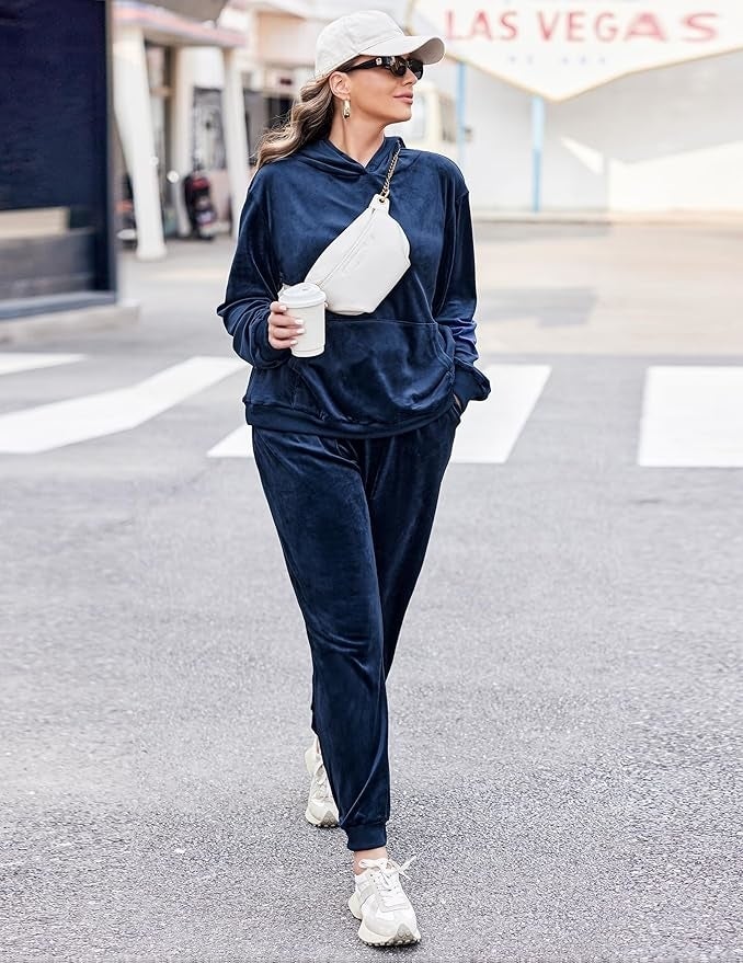  a navy bluish  velvet tracksuit, sneakers, achromatic  cap, crossbody bag, and holding a java  cup