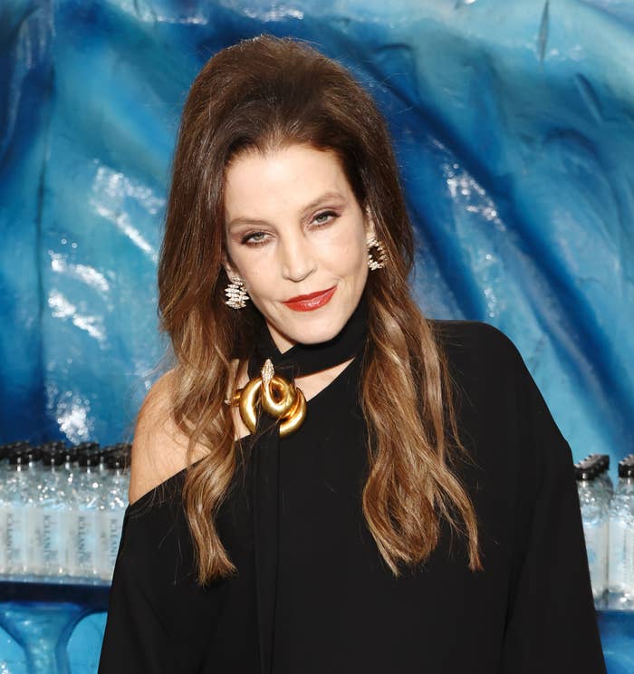 Lisa Marie Presley in an elegant off-shoulder gown standing in front of a blue textured background