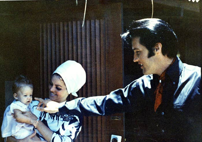 Elvis Presley and Priscilla Presley hold an infant Lisa Marie. Elvis is pointing at his daughter, and Priscilla is smiling