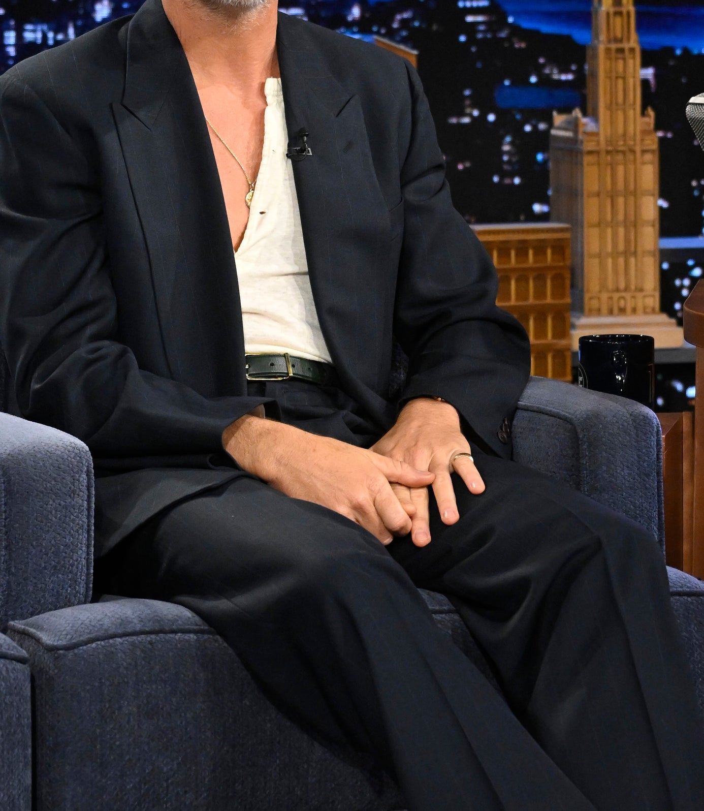 Chris Pine in a dark suit and light shirt smiles while sitting on a talk show set