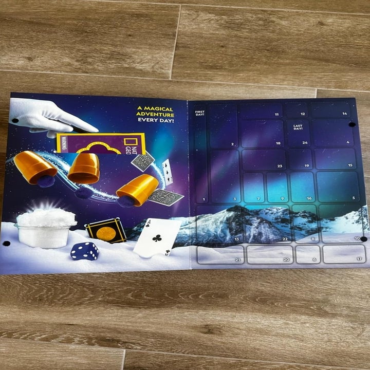 Magic-themed advent calendar with numbered doors, featuring props like cups, dice, cards, and a magic wand. Text says, "A magical adventure every day!"