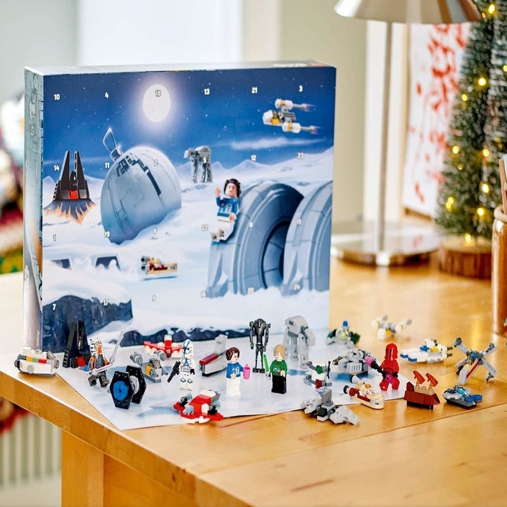 LEGO Star Wars Advent Calendar with mini LEGO Star Wars figures and ships displayed on a wooden table. Box shows scene from Star Wars universe