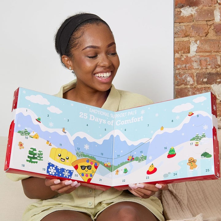 Woman smiles holding "Emotional Support Pals: 25 Days of Comfort" calendar with cartoon characters