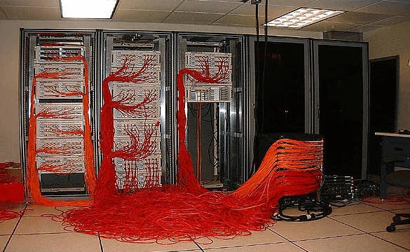 Server room with disorganized red cables spilling from racks onto the floor