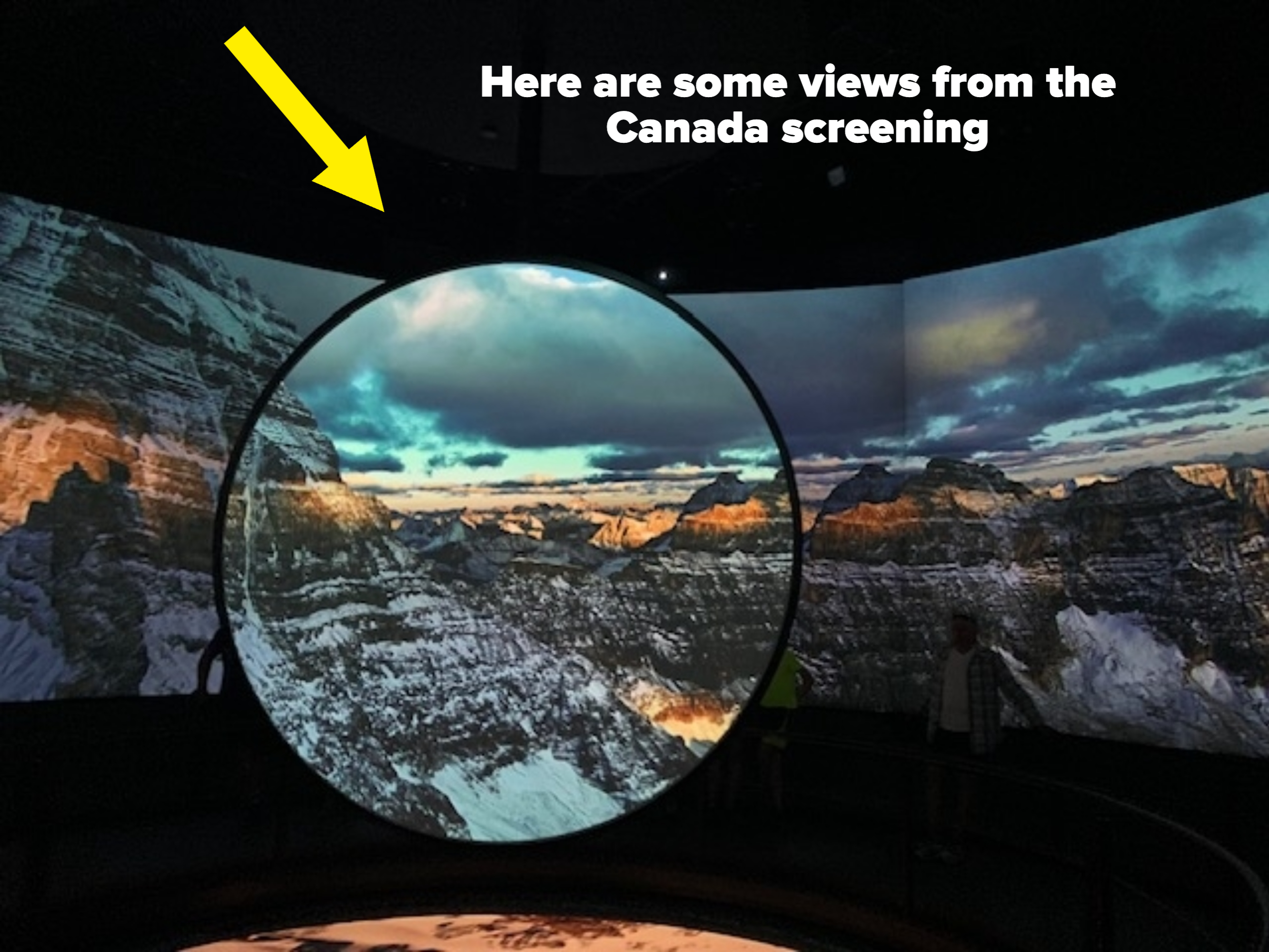 People observing a large projection of mountainous landscapes in a travel exhibit