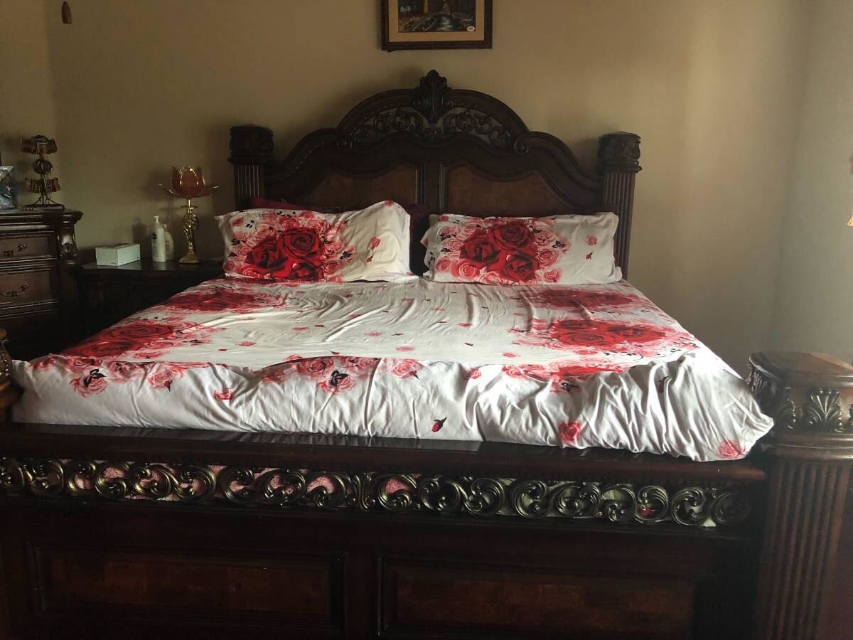 Ornate wooden bed with floral-patterned bedding and two pillows in a well-decorated bedroom