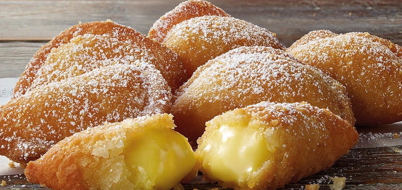 Fried pastries filled with creamy custard, dusted with powdered sugar, on a wooden surface