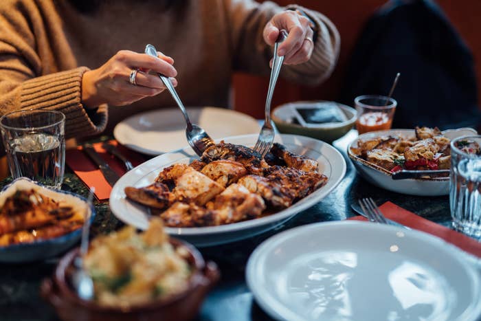 Person dining with various dishes, including a large plate of poultry or meat, surrounded by sides and sauces on a table