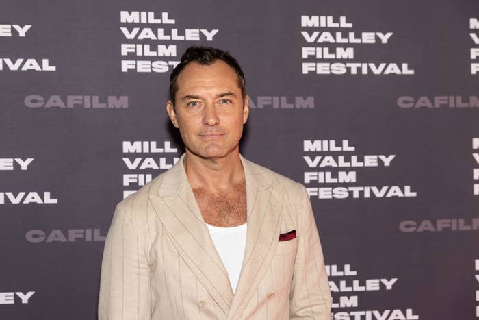 Jude Law in formal attire stands in front of a Mill Valley Film Festival backdrop