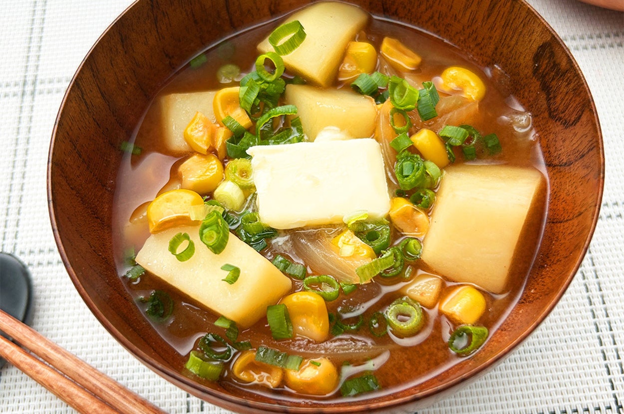 じゃがいも、バター、ネギ、コーンが入ったみそ汁が木製のボウルに盛られている。箸が横に置かれている。