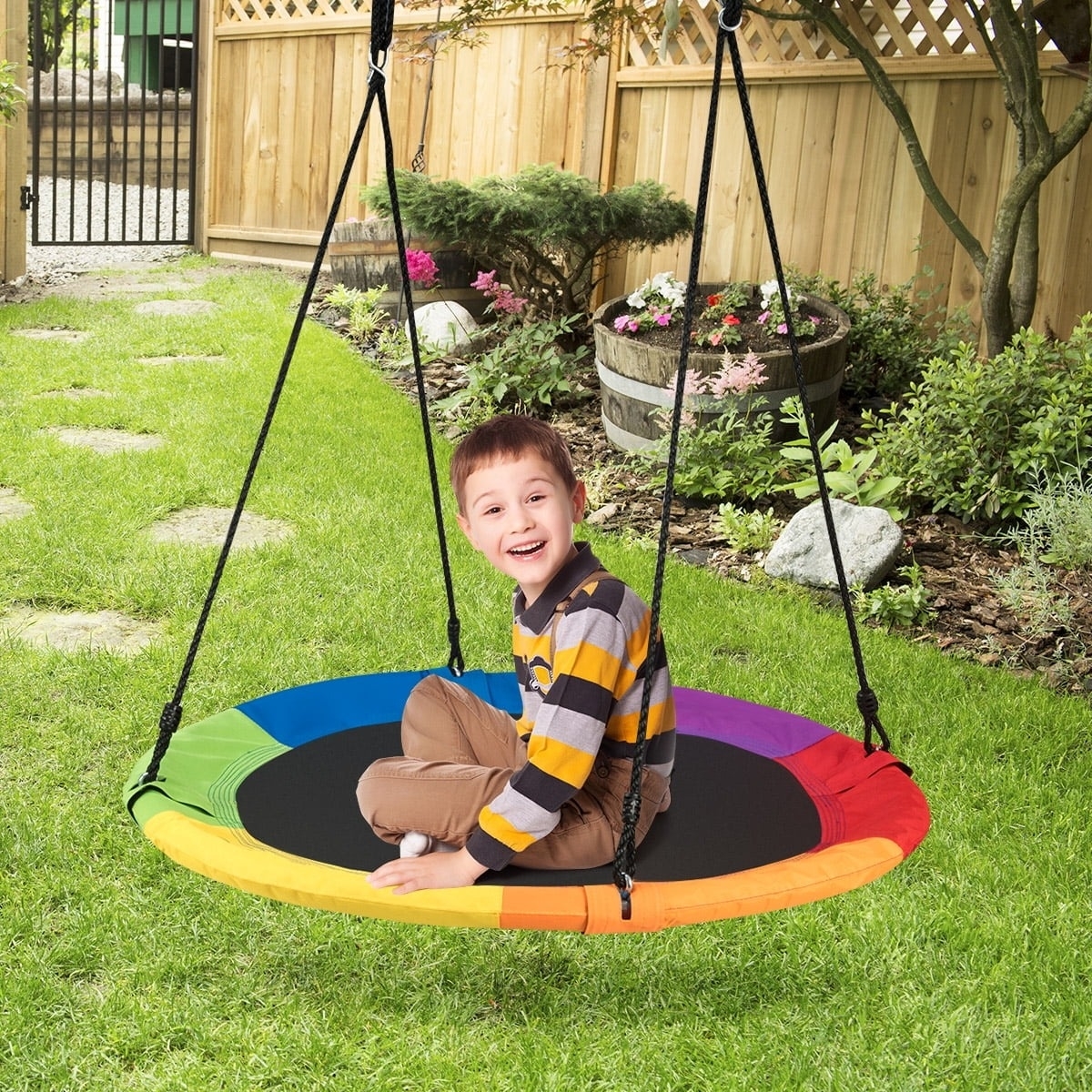Child smiling, sitting on a circular swing in a garden. The swing has a rainbow rim