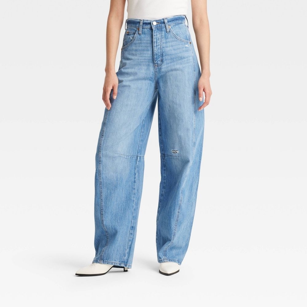 Person wearing wide-leg jeans and a white top, standing against a plain background; the jeans have a relaxed, casual fit