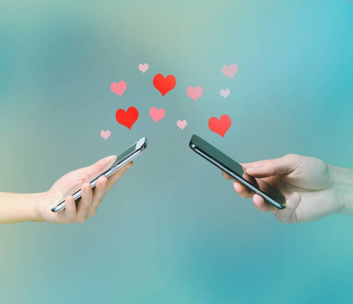 Two hands holding smartphones with hearts floating between them, symbolizing online dating or digital romance