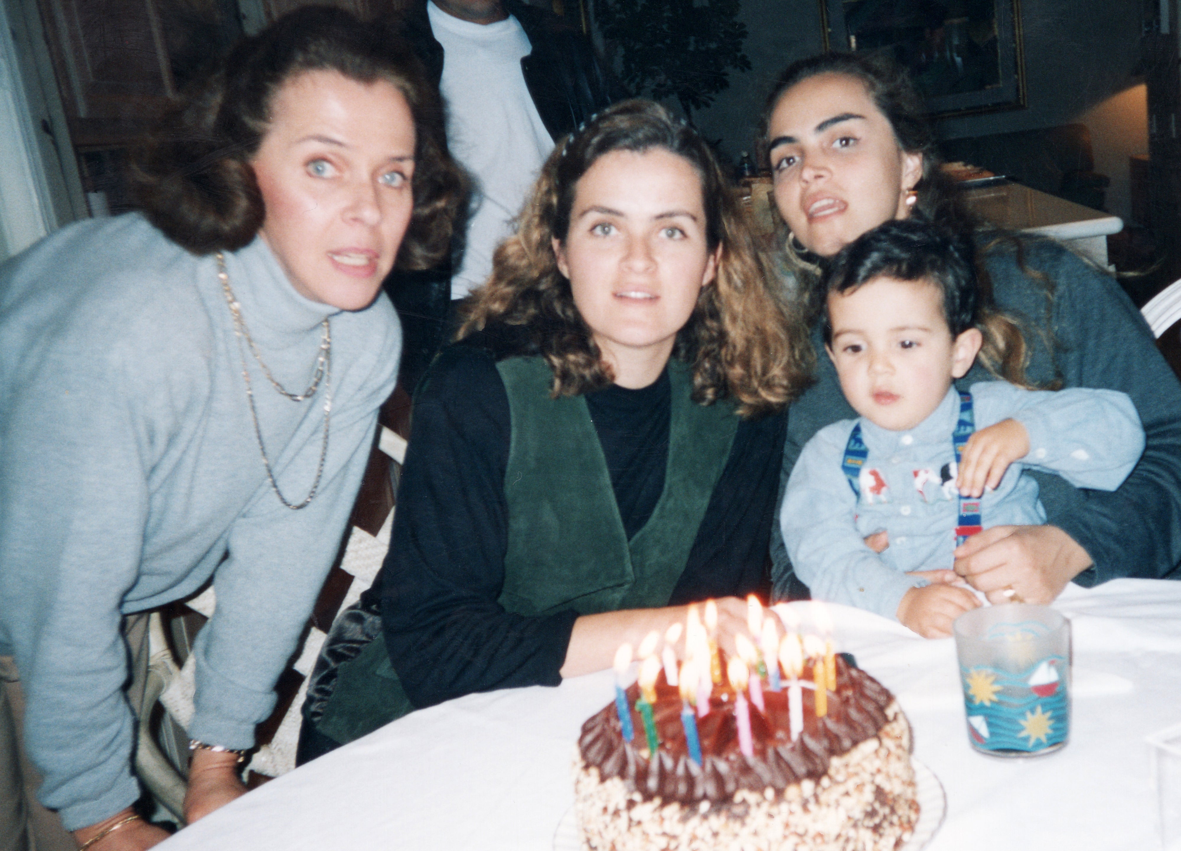 Four people gathered around a birthday cake with lit candles on a table