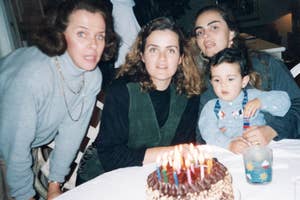 Four people gathered around a birthday cake with lit candles on a table