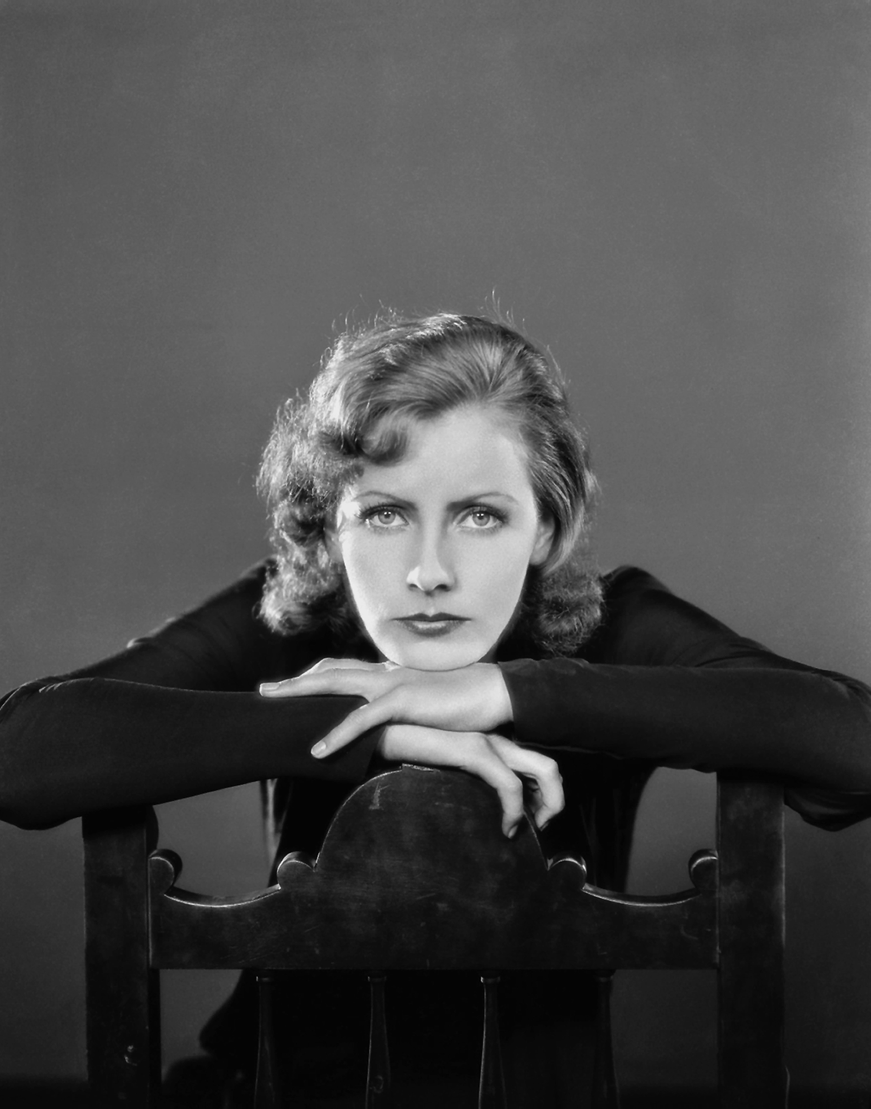 Actor from the classic film era, with wavy hair, leans on a chair, gazing directly at the camera