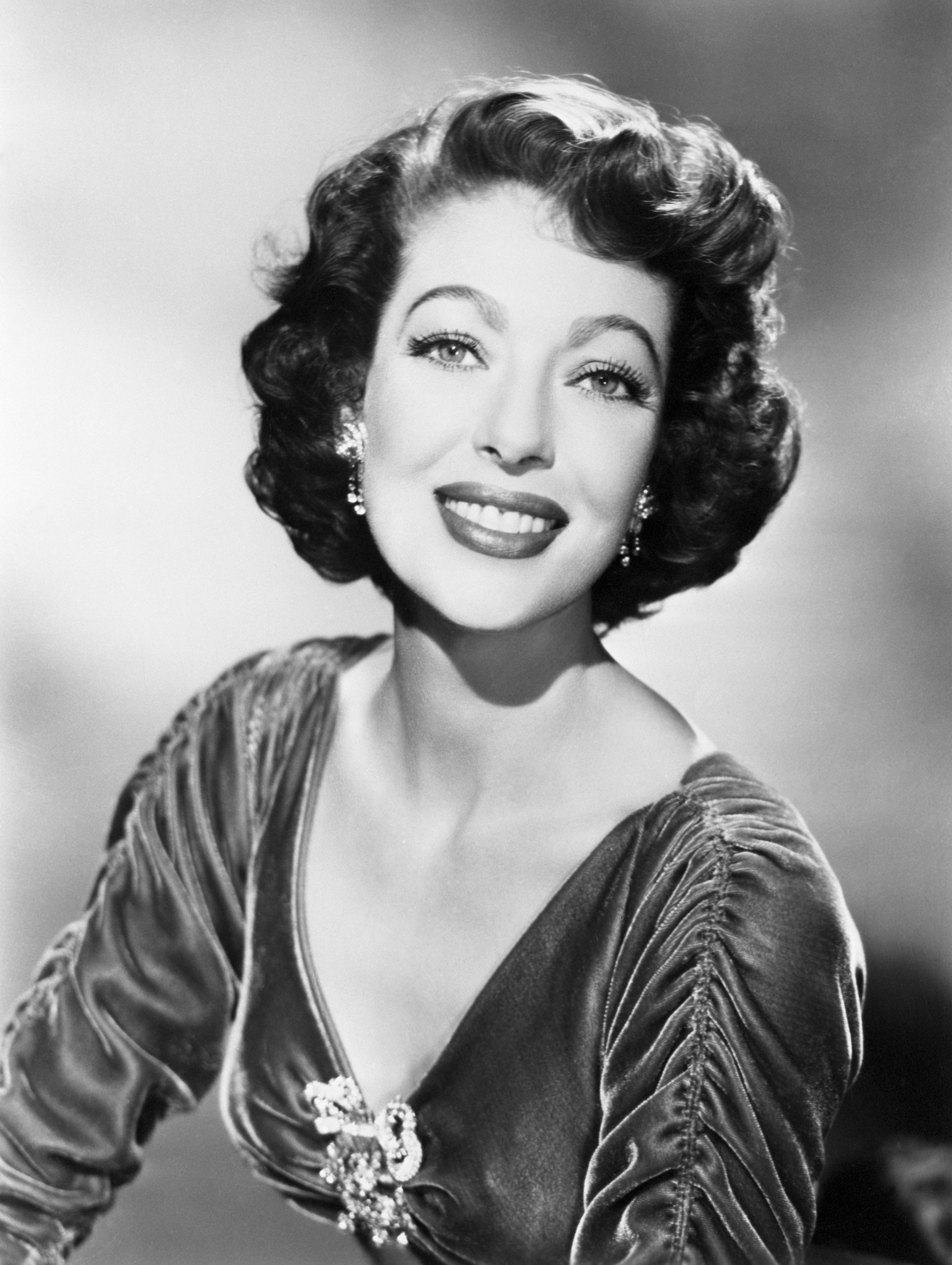 Vintage portrait of a smiling woman with wavy hair, wearing a velvet gown with a brooch, likely from the mid-20th century