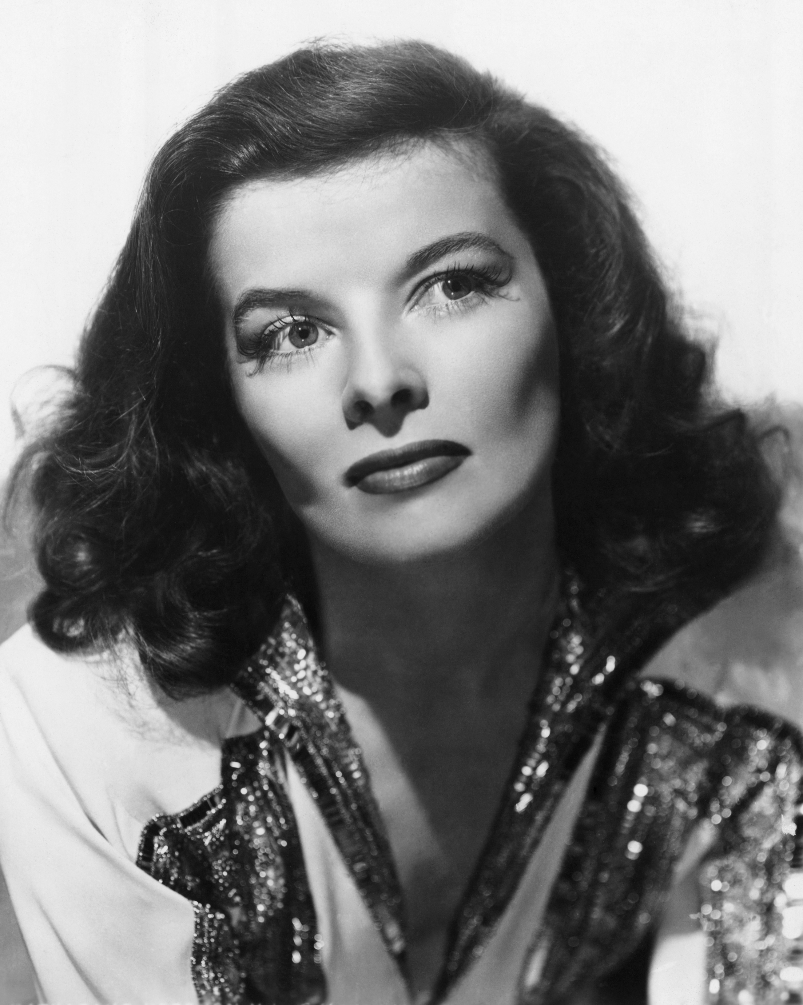 Actor in classic Hollywood style with wavy hair and sequin-embellished attire gazes thoughtfully off-camera in a dramatic portrait