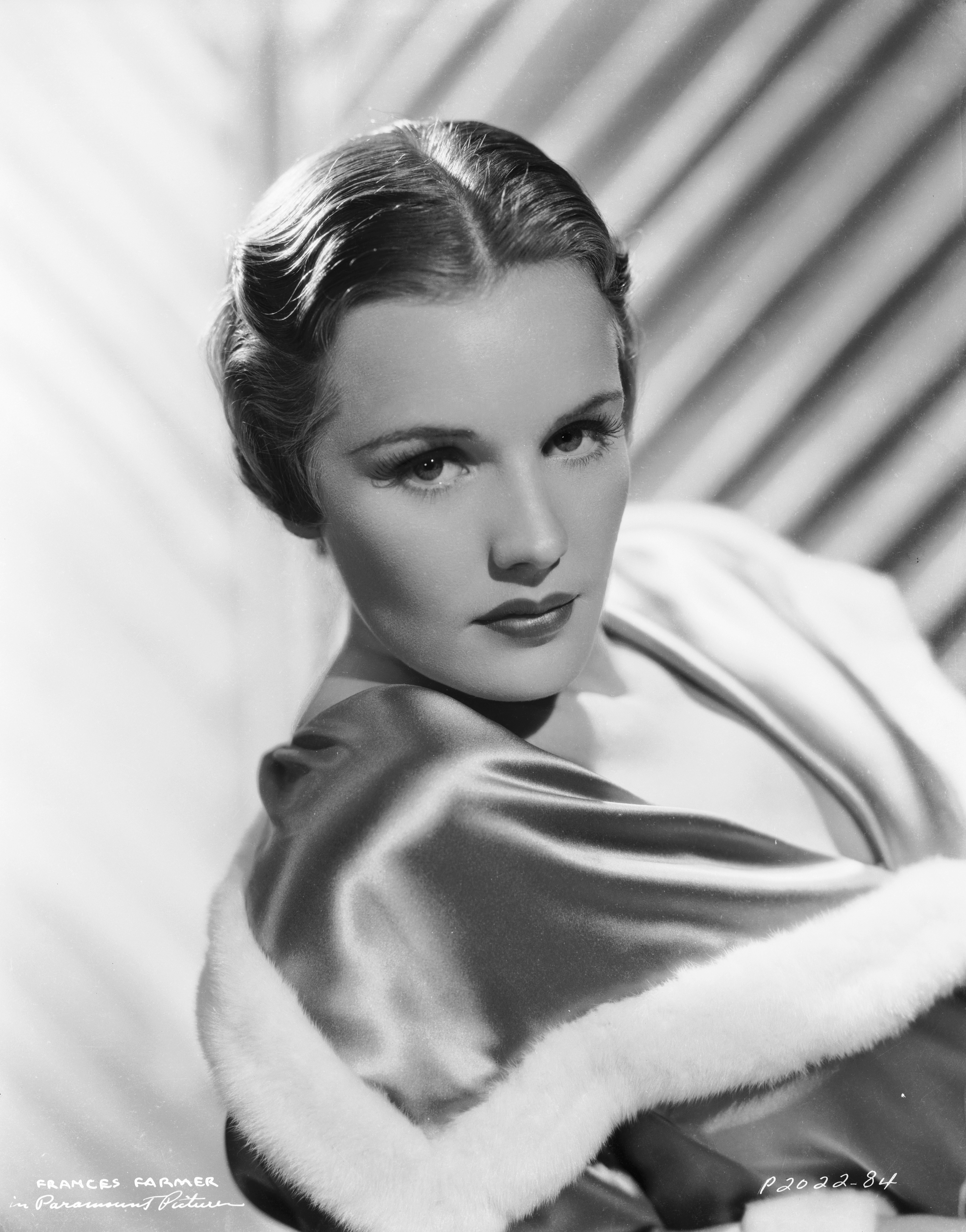 Vintage portrait of a woman in elegant 1940s attire with fur trim. She&#x27;s posed with a classic Hollywood glamour style