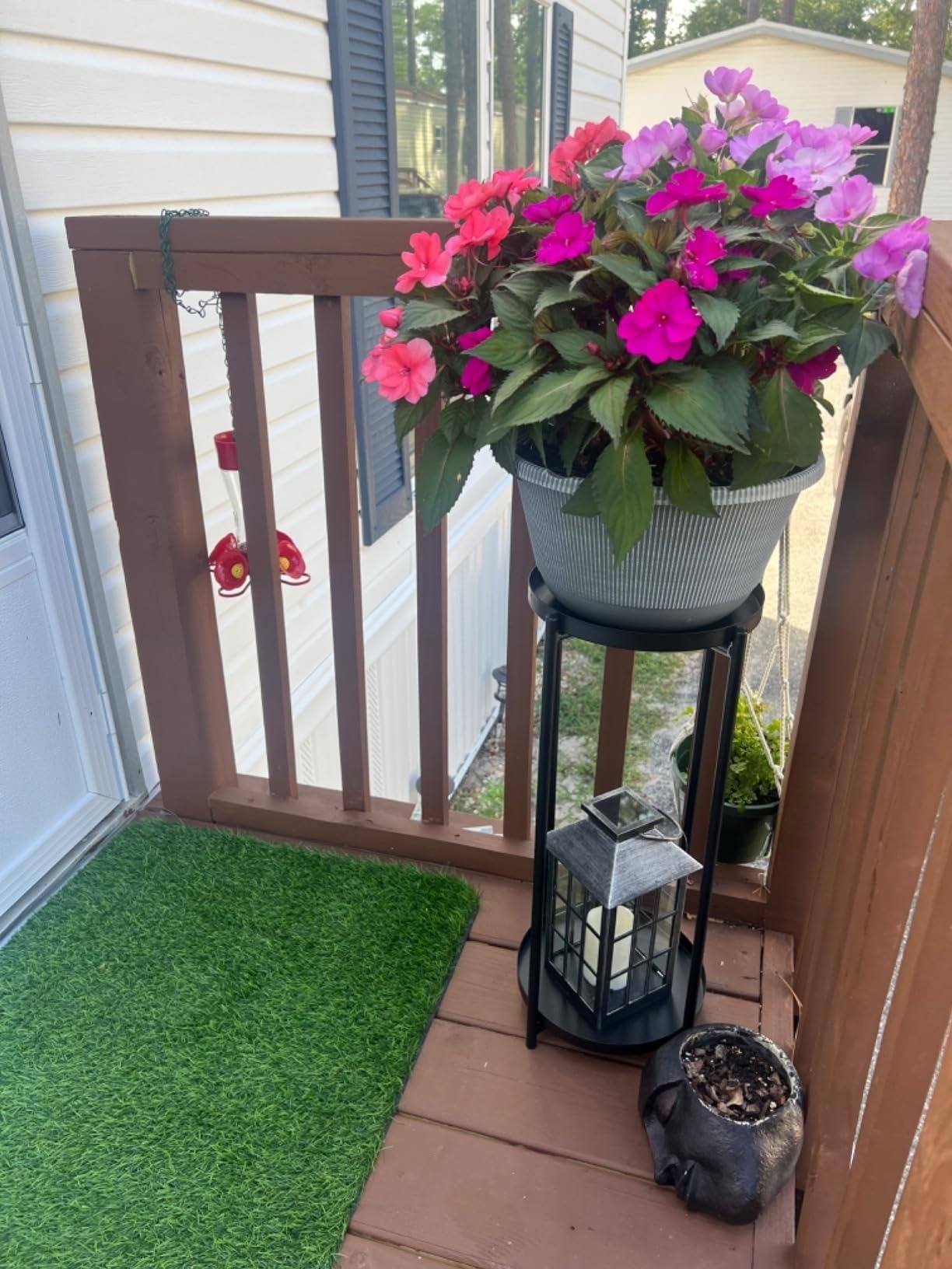 Potted pink and purple flowering plants on a porch, next to a black lantern and decorative items