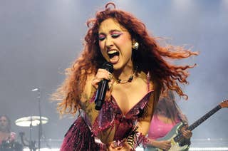 Chappell Roan passionately singing on stage, wearing a glittering, glamorous outfit, with band members playing instruments in the background