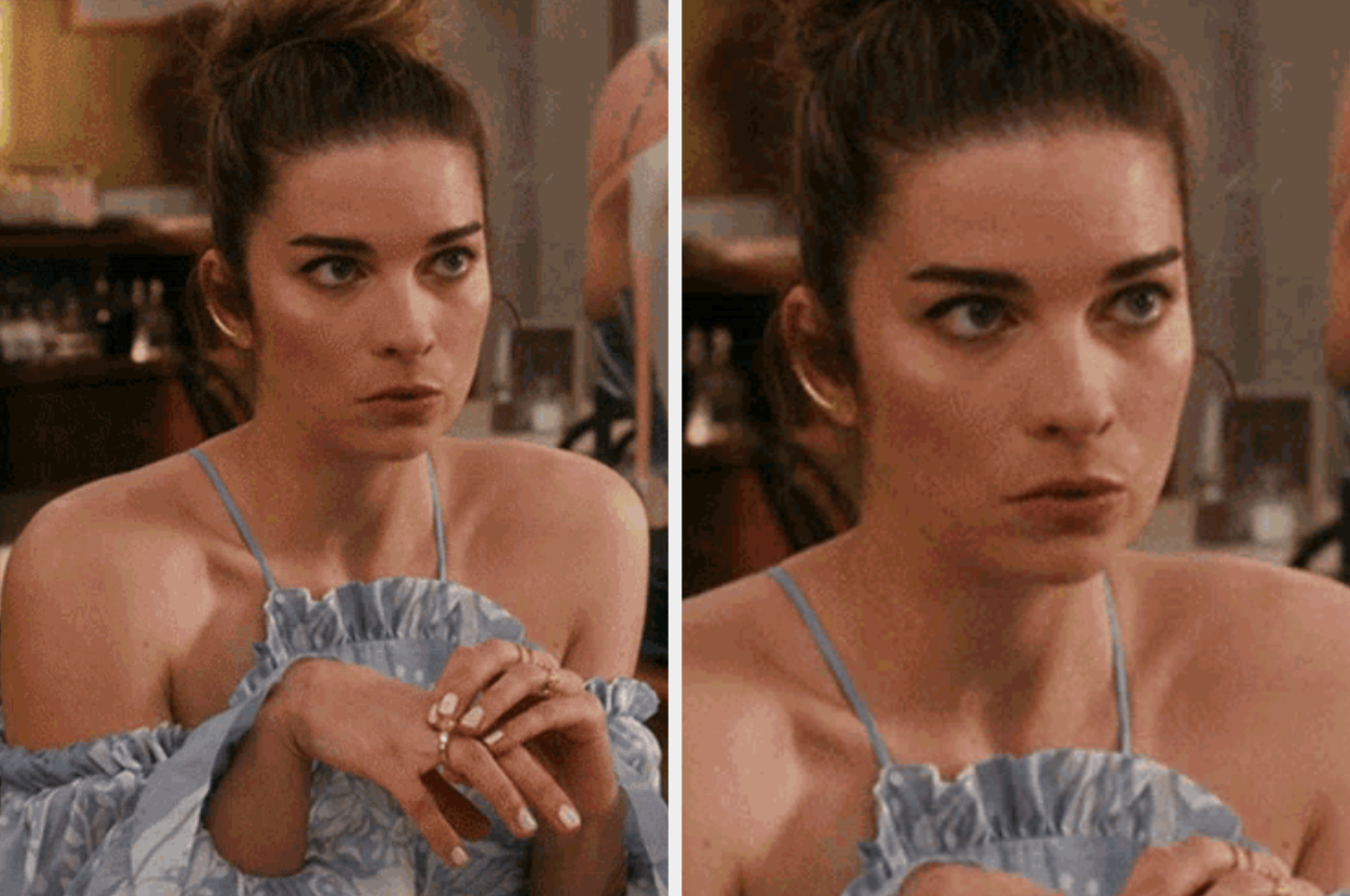 Person at a table, wearing a ruffled strapless dress, with hair in a bun, looking focused or concerned