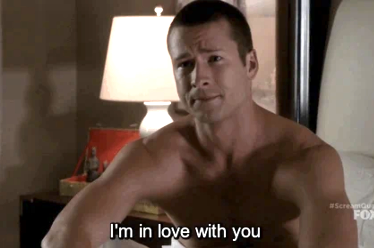 Man sitting on a bed, shirtless, expressing love. Background includes a lamp and framed picture