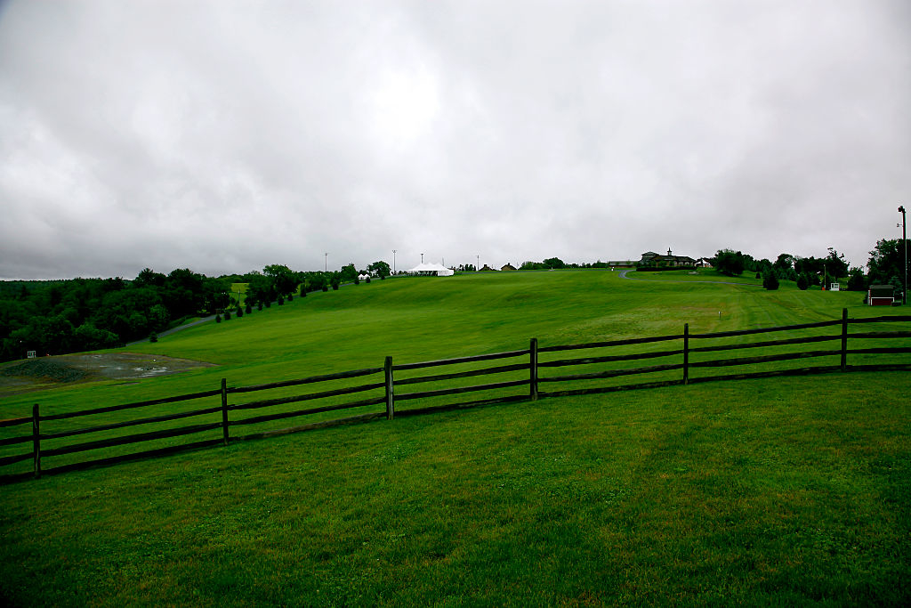 A rolling grassy hill with a wooden fence in the foreground and a cloudy sky above