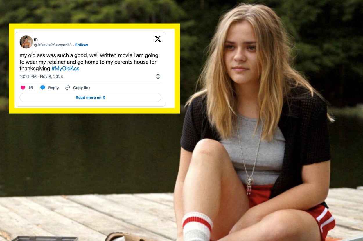 Person sitting on a dock by a lake, wearing a cardigan, t-shirt, and shorts, with sandals and socks, surrounded by trees